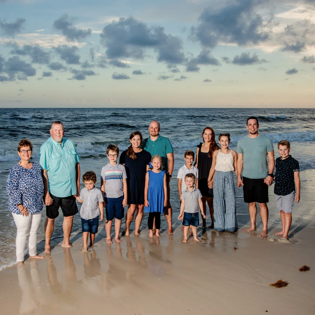 A large family portrait session in Fort Morgan, Alabama. The family standing by the water's edge, smiling, looking at the camera for a sunset photo session.