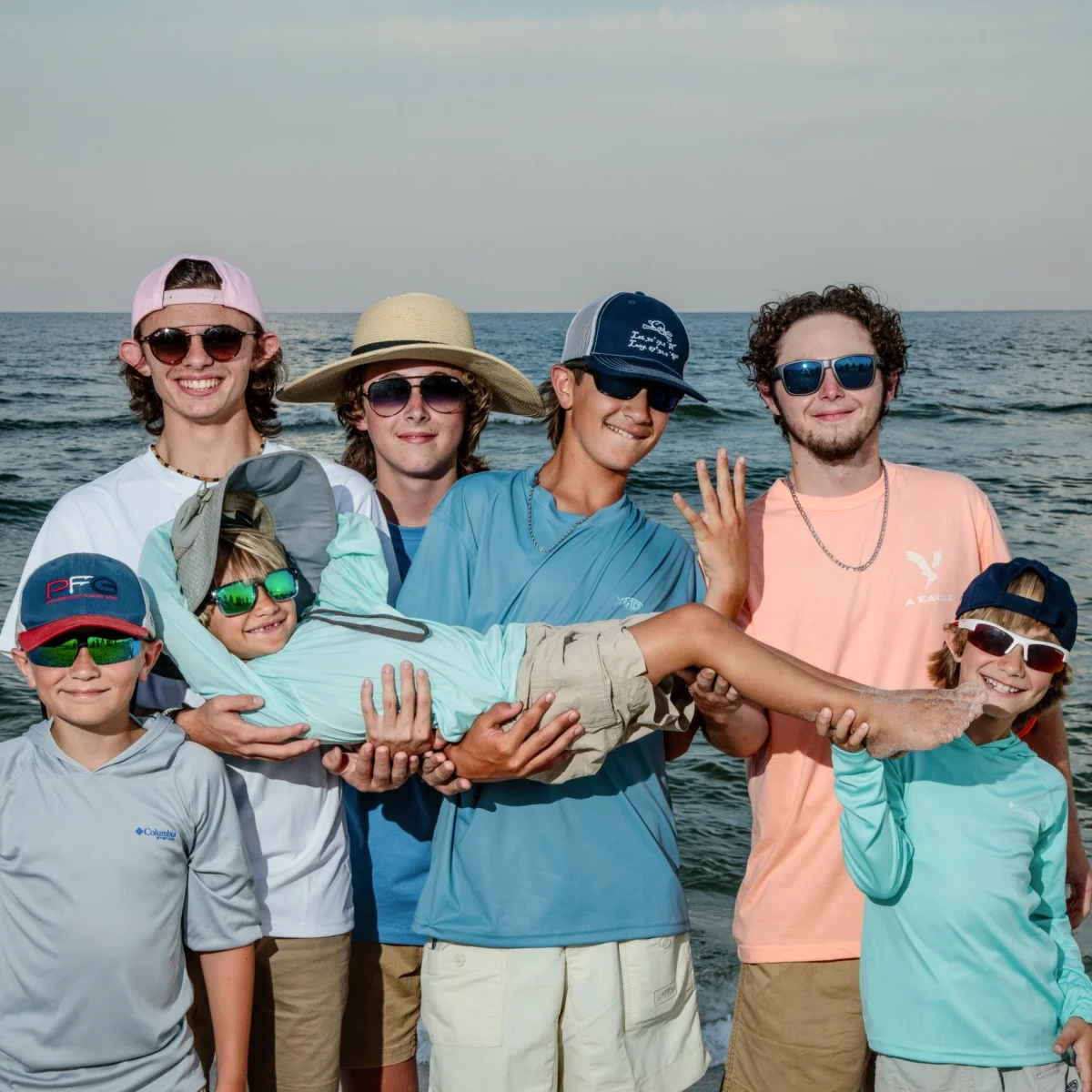 Seven young boys having a good time on the beach during a photo session standing by the water's edge in Fort Morgan, Alabama.