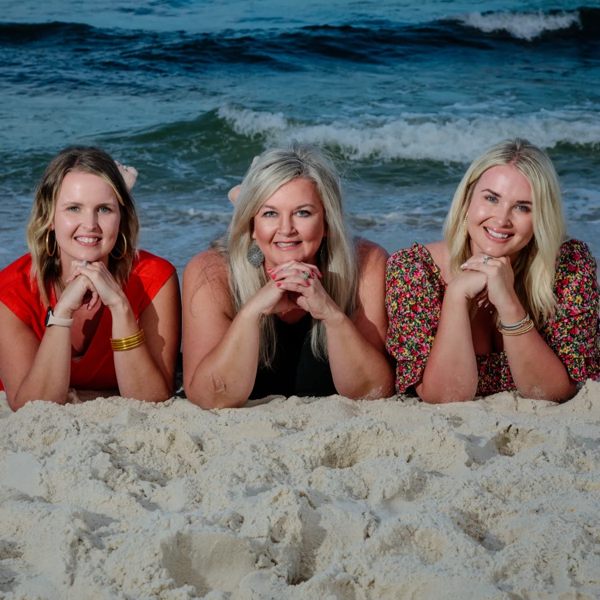 Three girls laying down on the beach looking at the camera during the photo session by the edge of the water in Fort Morgan, Alabama.