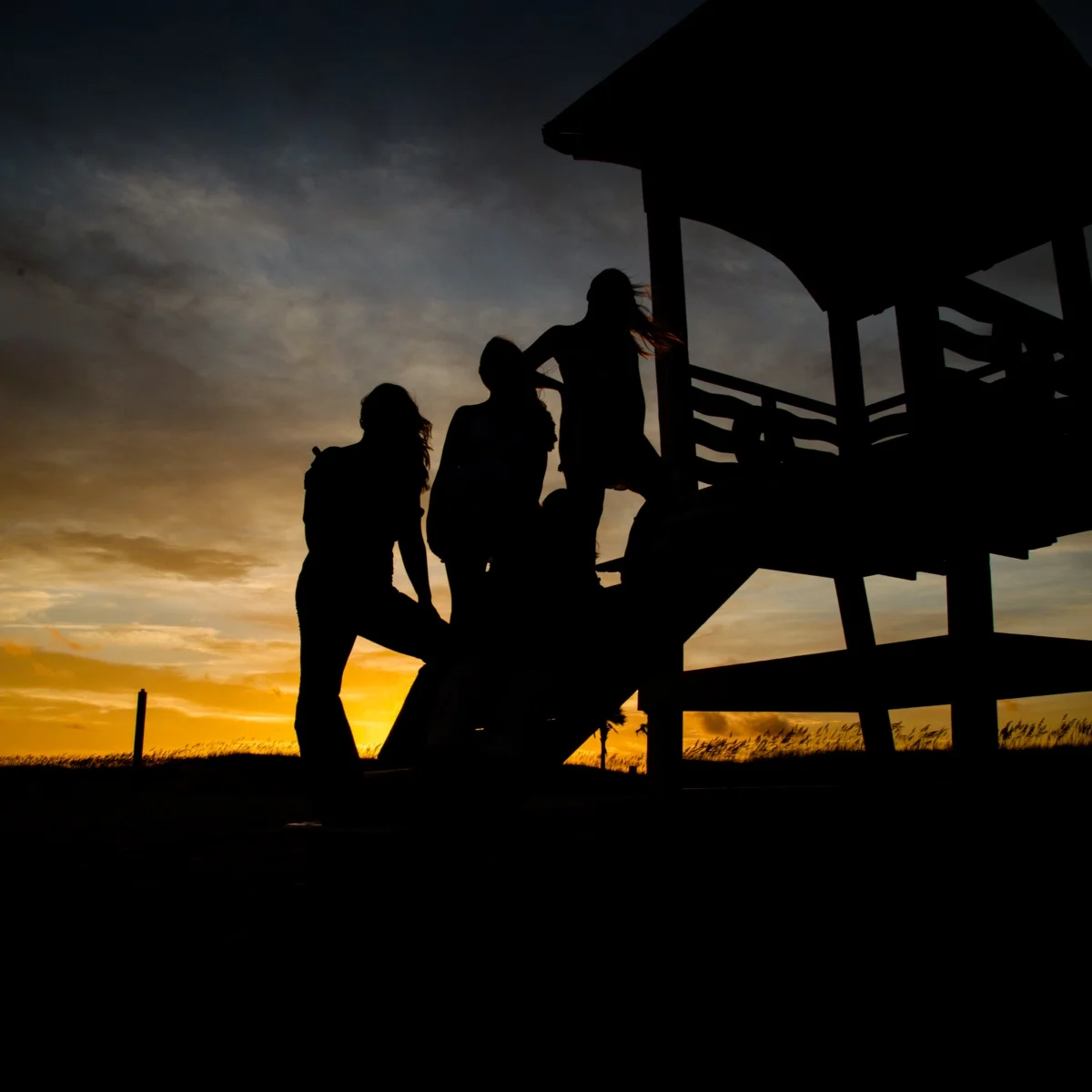 A silhouette photo of a family at sunset standing on the lifeguard tower on the beach.