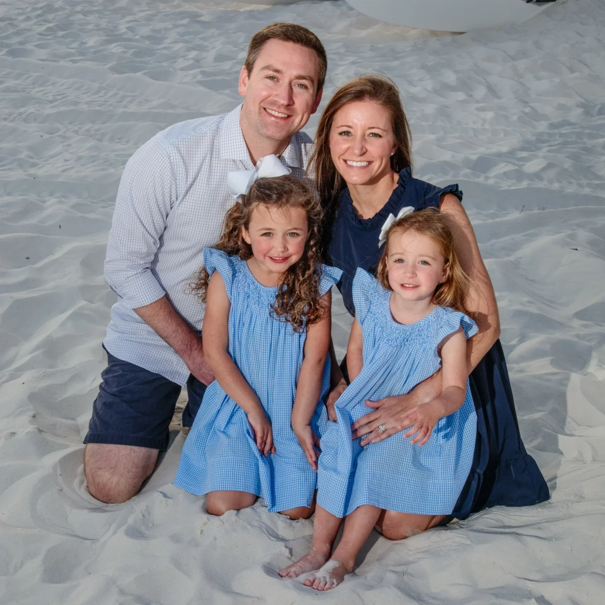 A family of four sitting in the sand on the beach in Fort Morgan, Alabama during a photo session.