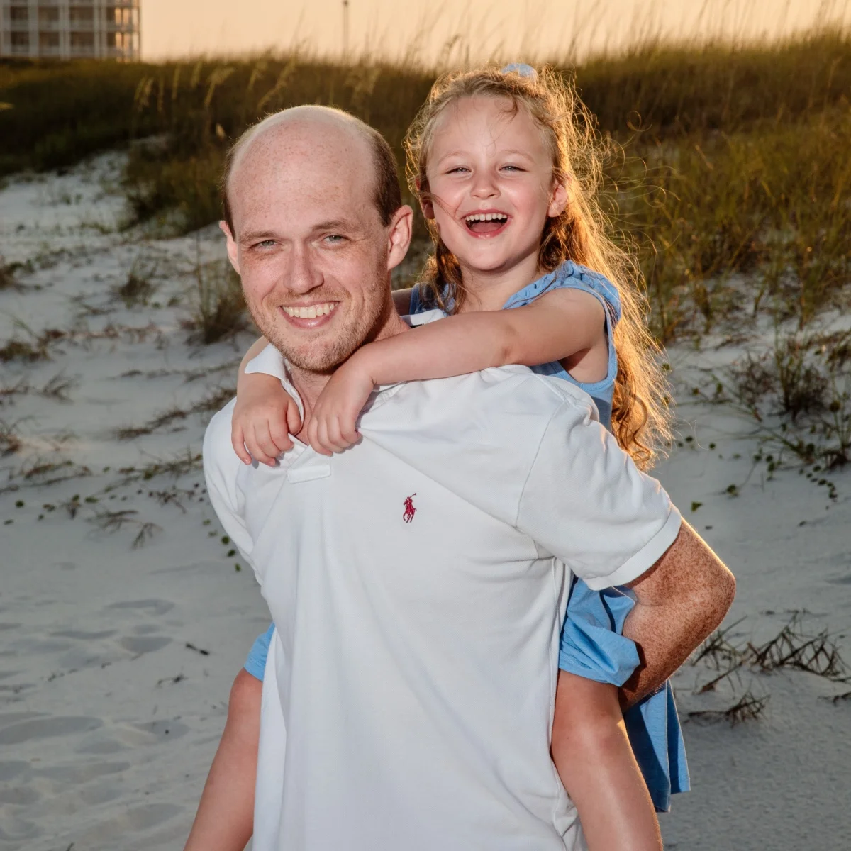 A dad with his daughter on his back having fun on the beach during a photo session in Fort Morgan, Alabama.