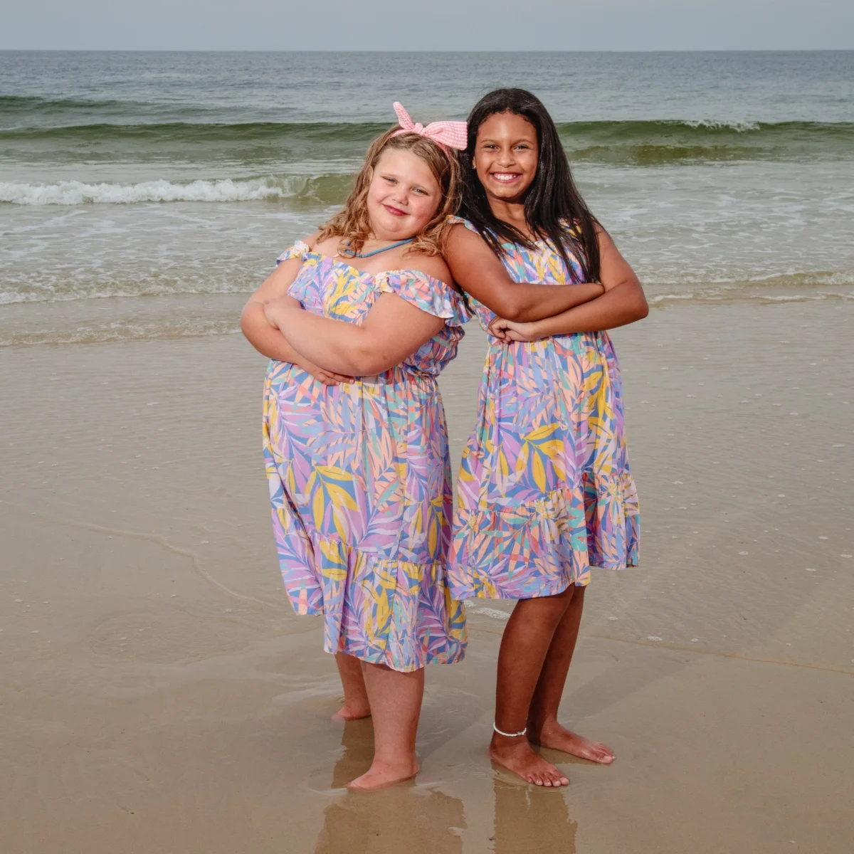 Two girls standing back to back on the by the water's edge for a photo session in Fort Morgan, Alabama.
