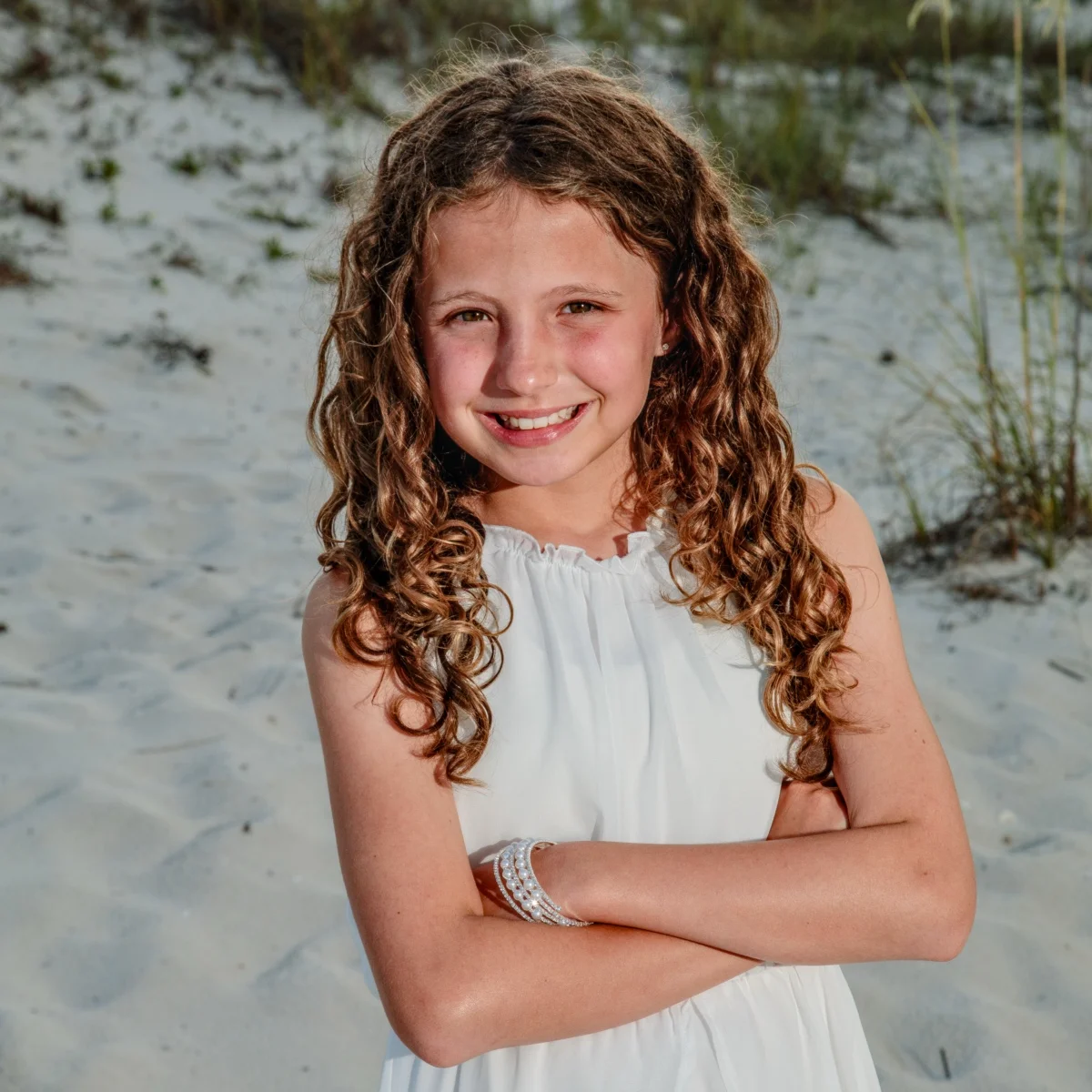 A photo of a happy young girl standing on the beach during a photo session in Fort Morgan, Alabama.