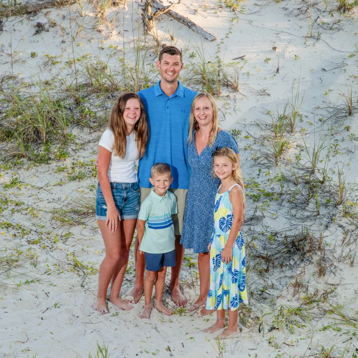 A happy family of five having their photos taken on the beach in Fort Morgan, Alabama by the sand dunes.