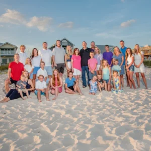 A large family reunion photo of everyone standing and sitting in the sand in Fort Morgan, Alabama.
