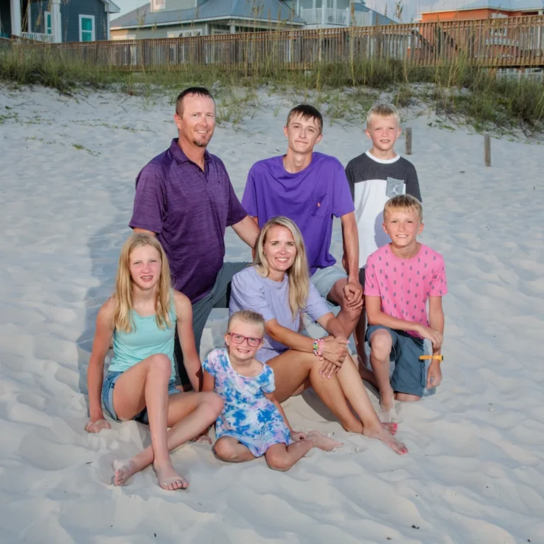 A family of seven having a beach portrait done sitting in the sand in Fort Morgan, Alabama.