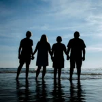 A silhouette photo of a family of four during a photo session standing in the water.