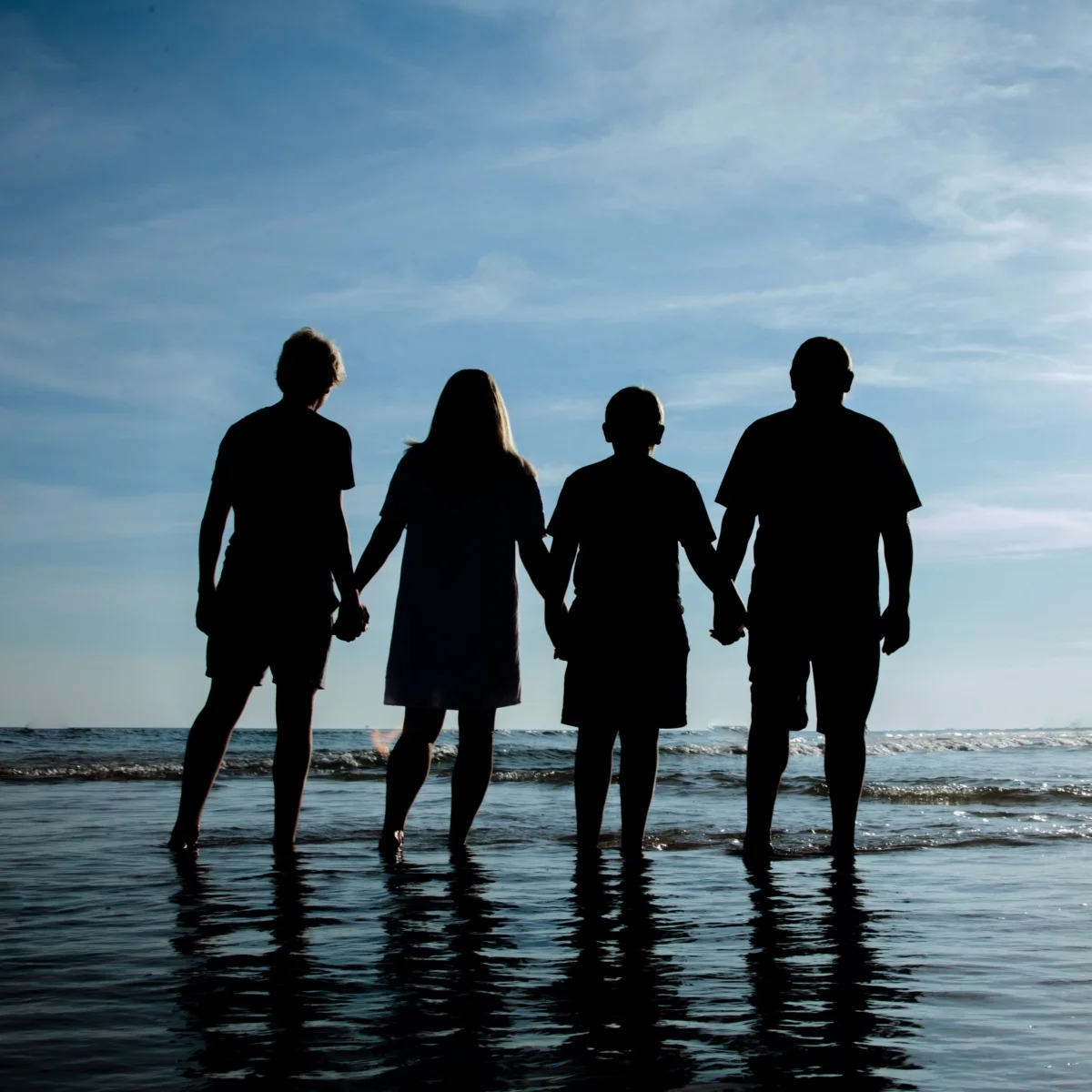 A silhouette photo of a family of four during a photo session standing in the water.