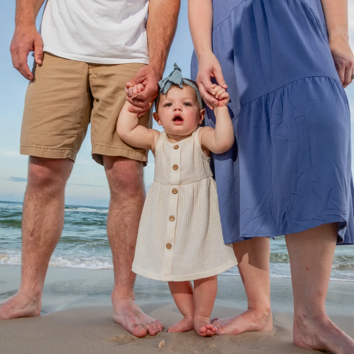 Close-up of a baby standing with its parents by the water's edge in Fort Morgan, Alabama.